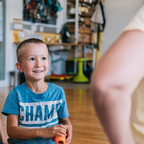 Ein Bub hält ein Spielzeug in der Hand und sieht dabei lachend Angelika Reichartzeder an.